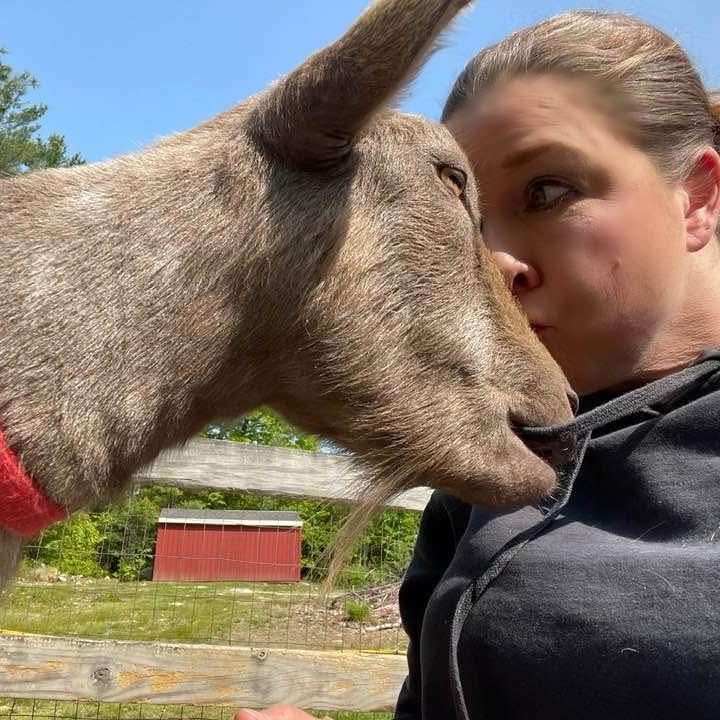 Lisa giving one of her goats a kiss on the nose by the paddock fence